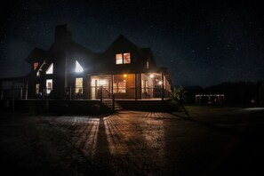 Una casa grande de dos pisos con múltiples ventanas y un porche bien iluminado.