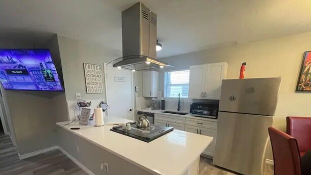 A modern kitchen with a central island, stainless steel appliances, and a flat-screen TV mounted on the wall. - Right by AT&T, Rangers stadium (Arlington)