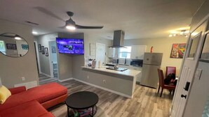 A modern living room with a red sofa, a round coffee table, and a kitchen area with white cabinets and a stainless steel refrigerator. - Right by AT&T, Rangers stadium (Arlington)