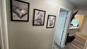 A hallway with three framed artworks on the wall, a door, and a desk with a computer. - Right by AT&T, Rangers stadium (Arlington)
