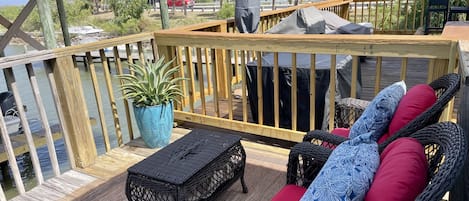 A wooden deck with wicker furniture, a potted plant, and a view of the water and palm trees.