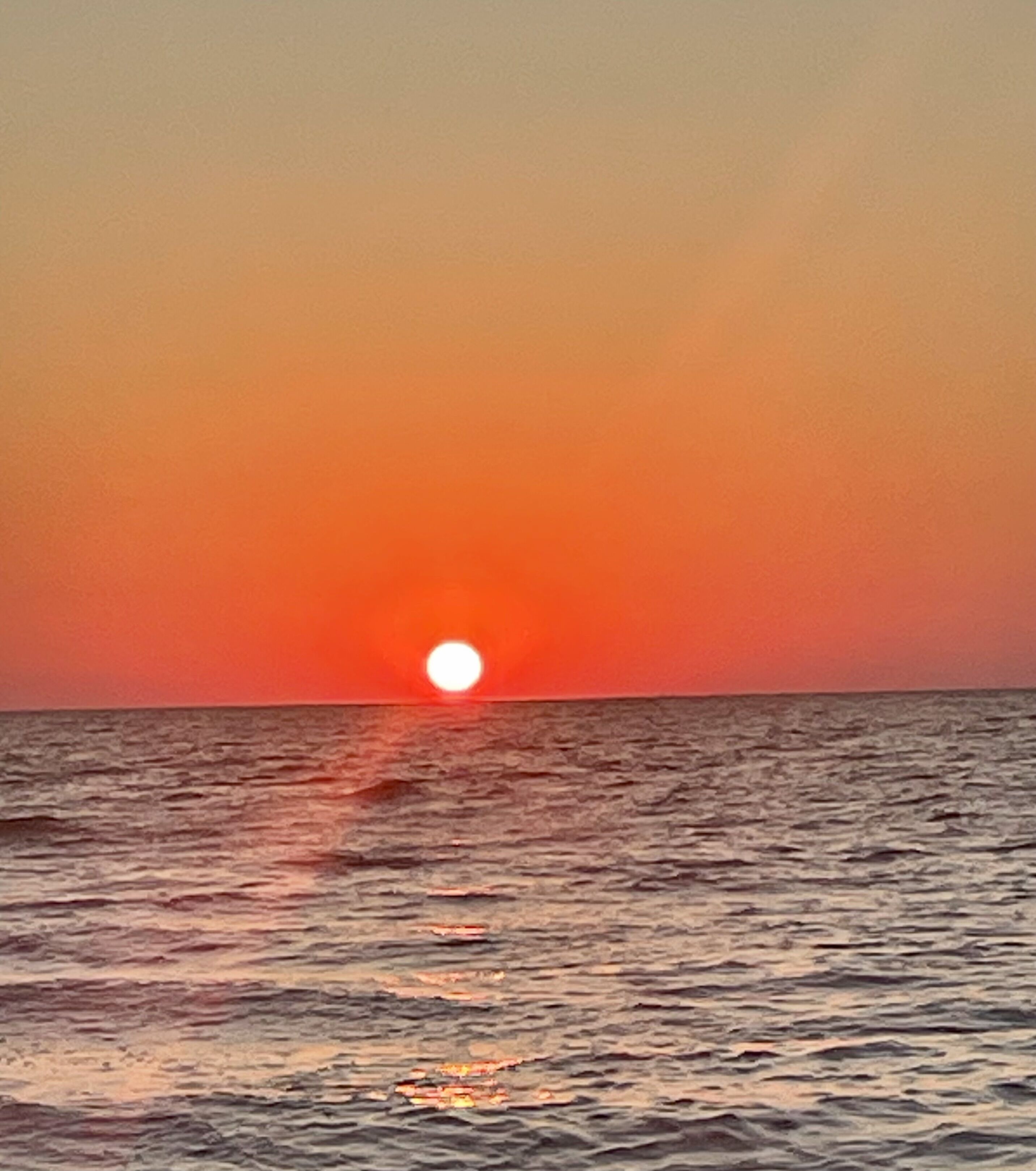 A sunset over the ocean with calm waters reflecting the sky.