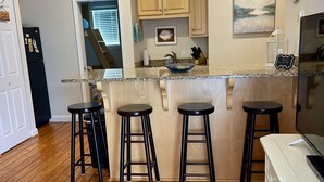 A kitchen with wooden cabinets, a granite countertop, and four bar stools. - Cute waterfront bungalow, tons of amenities, a small gated fishing community! (Dauphin Island)