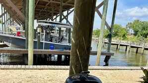 A barbecue grill on a concrete surface under a wooden structure with a boat docked in the background. - Cute waterfront bungalow, tons of amenities, a small gated fishing community! (Dauphin Island)