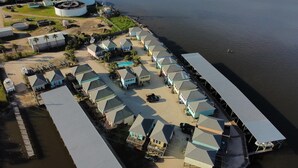 An aerial view of a coastal hotel with multiple buildings, a swimming pool, and a dock extending into the water. - Cute waterfront bungalow, tons of amenities, a small gated fishing community! (Dauphin Island)