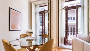 Un espace repas moderne avec une table en verre et des chaises jaunes, une œuvre d’art encadrée au mur et une vue sur le balcon extérieur.