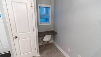 A hallway with a white door, a window with blinds, a dark wooden bench, and a white chair.