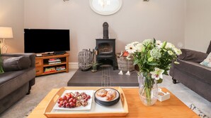 A living room with a television, a fireplace, a sofa, and a coffee table with snacks. - Church View (Grange-over-Sands)