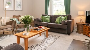 A living room with a sofa, armchair, coffee table, and a TV stand. - Church View (Grange-over-Sands)