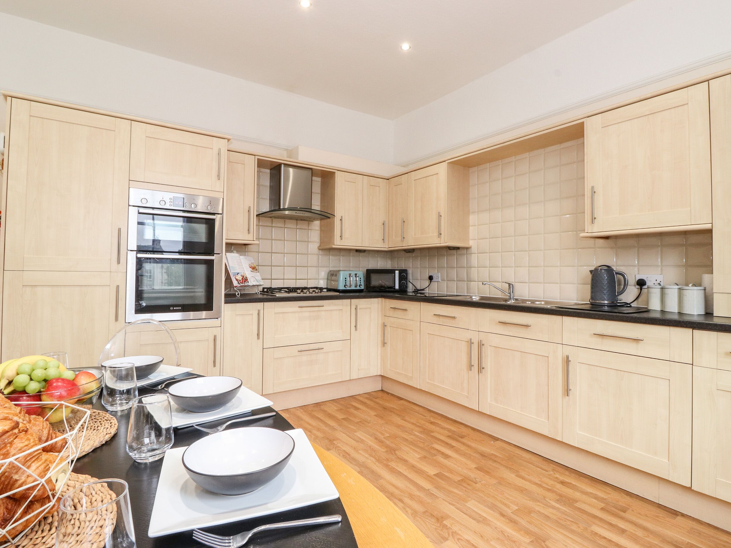 A modern kitchen with light wood cabinets, stainless steel appliances, and a black countertop.
