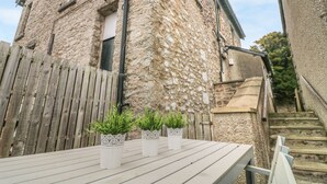 A stone building with a wooden fence and a wooden deck with potted plants. - Church View (Grange-over-Sands)