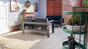 Une terrasse avec un canapé, une petite table et un ensemble de plantes en pot.