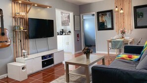Un salon moderne doté d’un téléviseur à écran plat, d’une guitare, d’un canapé, d’une table basse et d’un coin repas avec une petite table et des chaises.