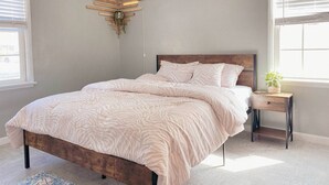 Une chambre à coucher comprenant un lit, une table de chevet, une étagère fixée au mur et une fenêtre.