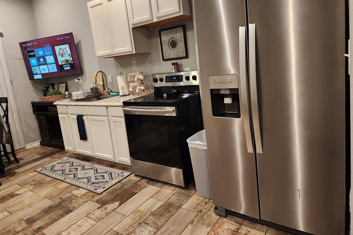 A kitchen with white cabinets, a stainless steel refrigerator, a stove, and a water dispenser.