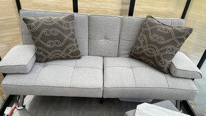 A grey sofa with patterned cushions and a small wooden side table with cork pads. - Cedar Springs Greenhouse (Decorah)