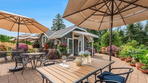 Eine Terrasse im Freien mit Holztischen und -stühlen, großen Sonnenschirmen und Topfpflanzen.