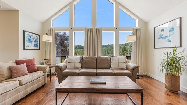 Ein großzügiges Wohnzimmer mit hohen Decken, großen Fenstern, einem Ledersofa, einem Holztisch und einem Blumentopf.