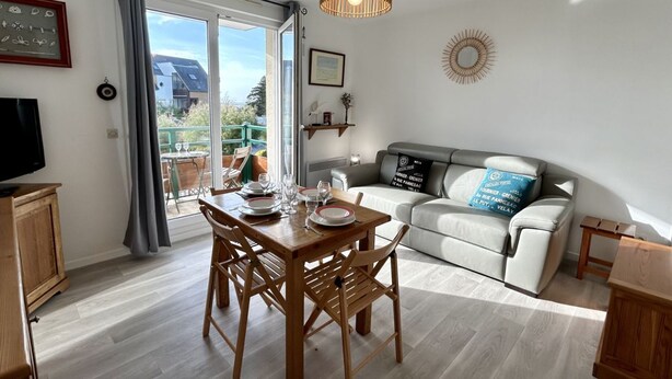 A living room with a dining table, chairs, a sofa, a TV, and a balcony with a view.