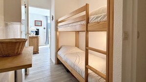 A bunk bed with a wooden frame, a wicker basket on a table, and a door leading to another room.