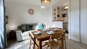 A dining area with a wooden table set for four, a grey sofa, and a kitchen in the background.