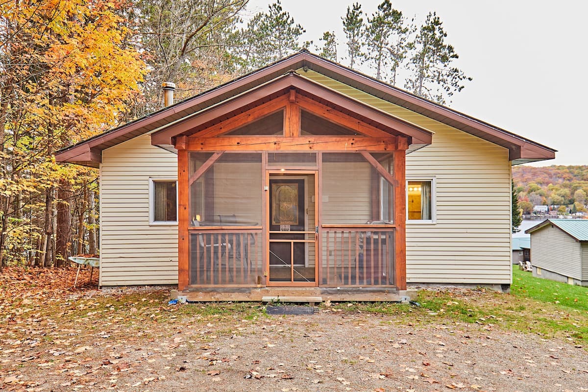 Une petite cabane à un seul étage, dotée d’un porche à l’avant, d’une porte avec un panneau de verre et d’une cheminée.