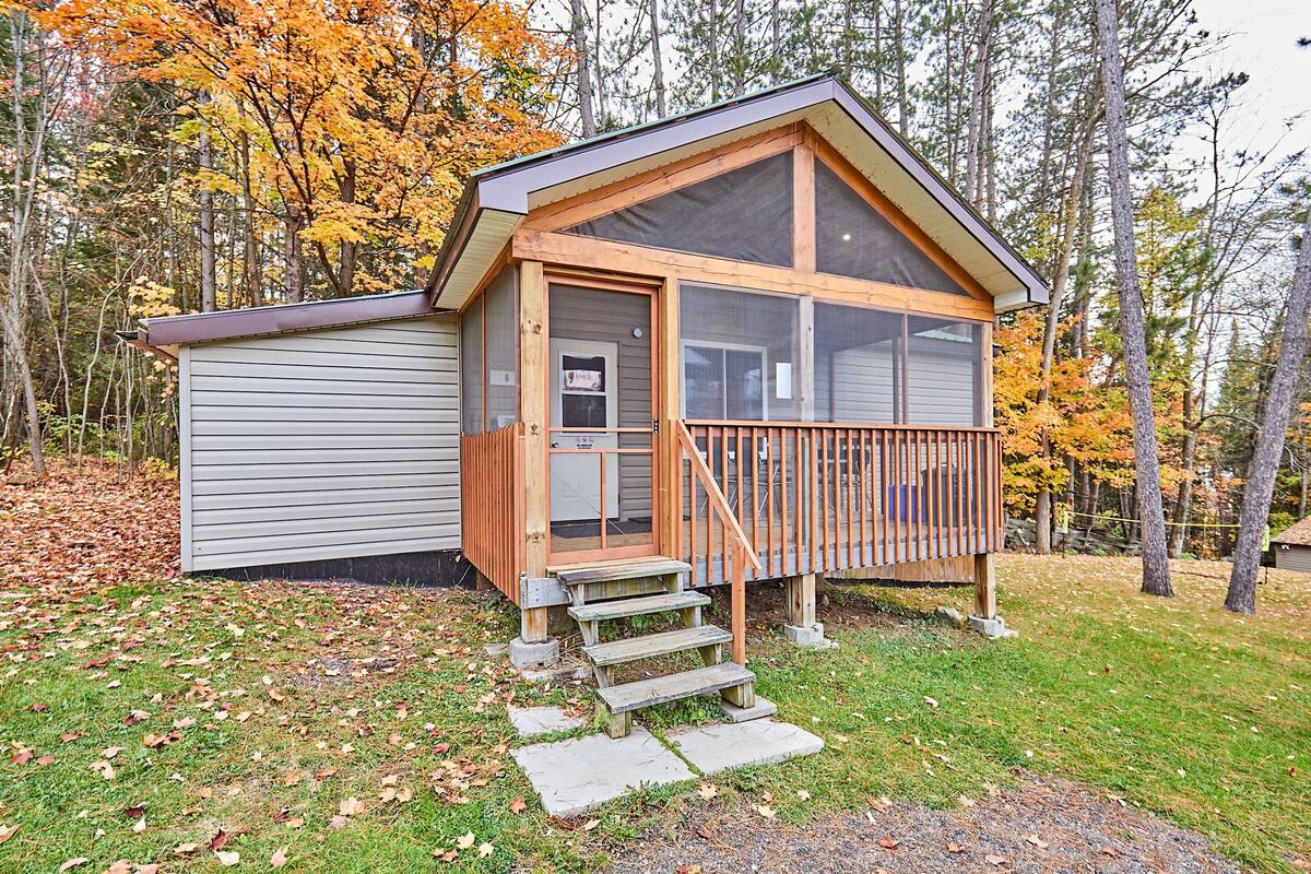 Une cabane dotée d’une terrasse en bois, d’une porte d’entrée et d’un petit escalier menant à celle-ci.
