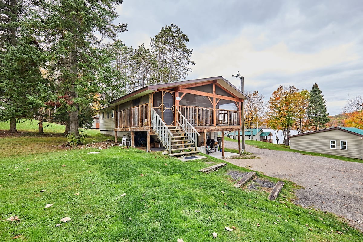 Une cabane en bois dotée d’un porche et d’un escalier, entourée d’arbres et bordée d’une allée en gravier.