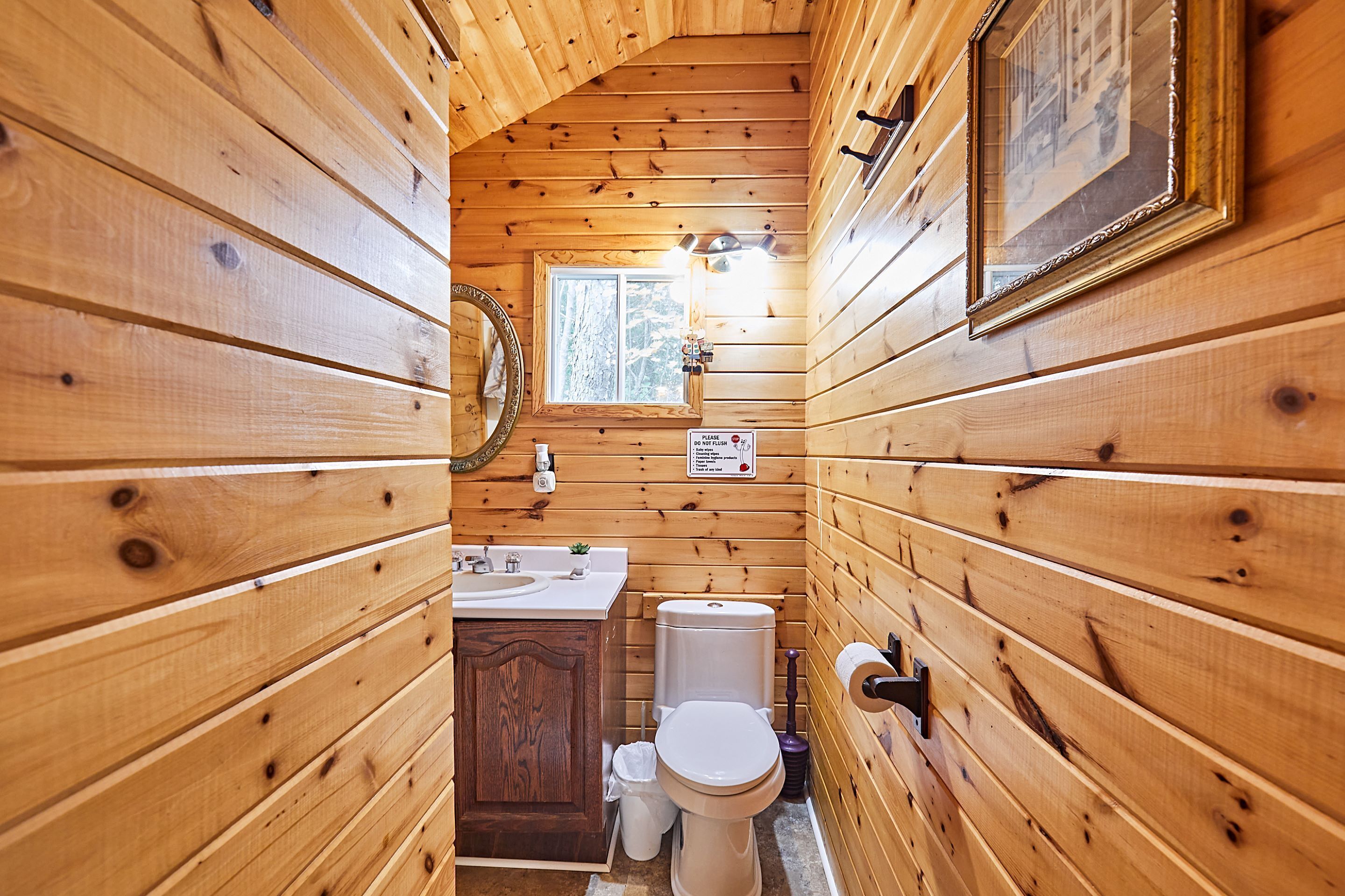 A wooden cabin bathroom with a toilet, sink, and vanity.