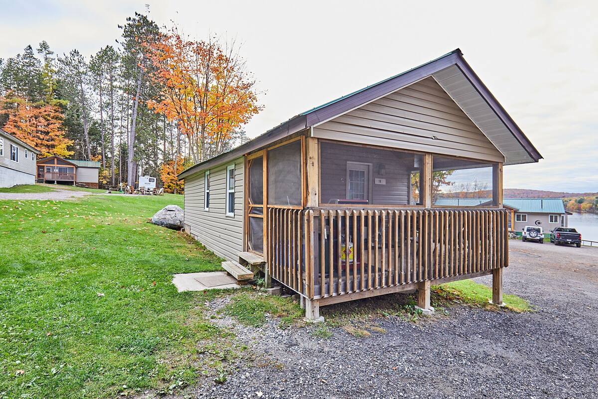 Une petite cabane avec une véranda, une terrasse couverte et une vue sur un lac.