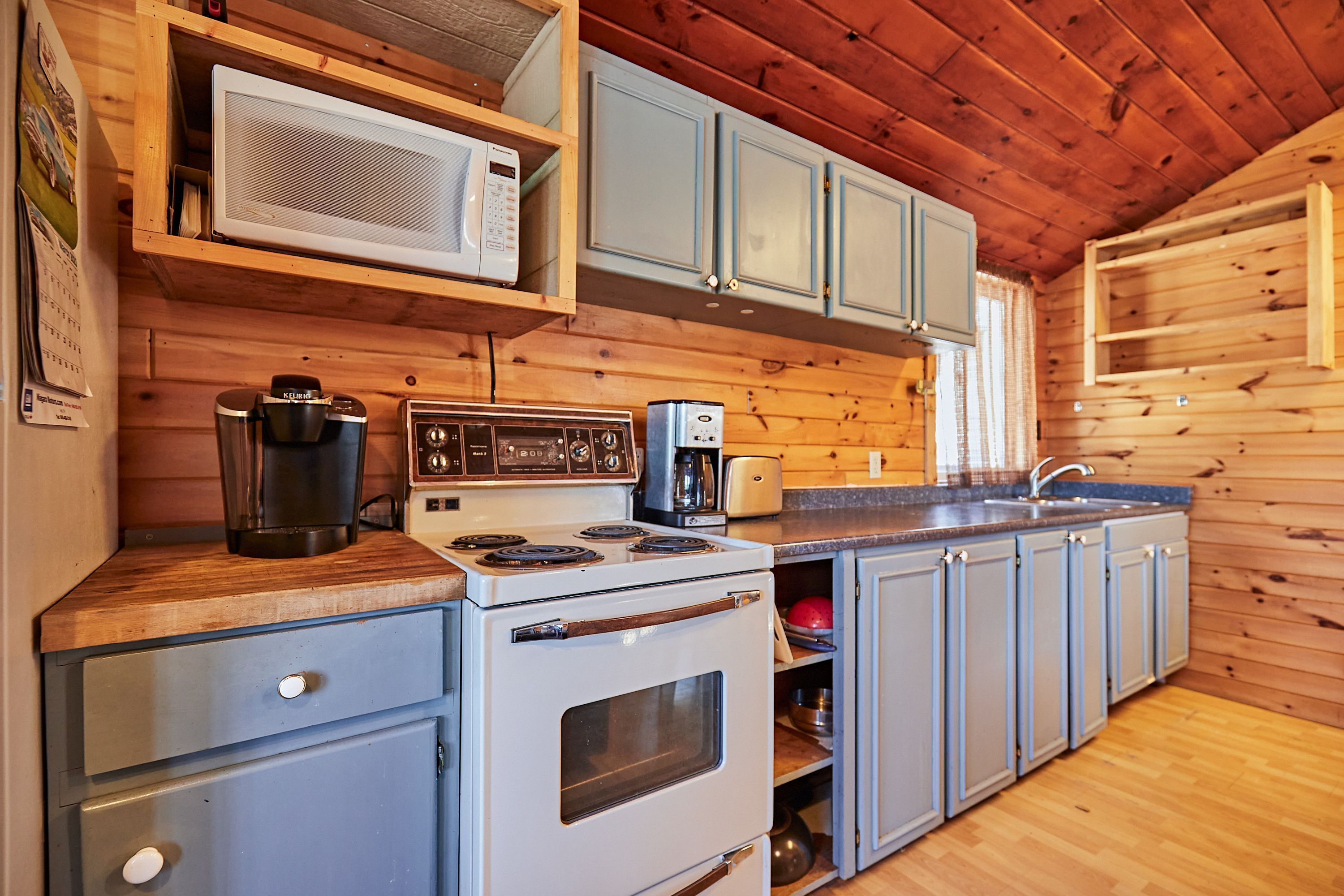 A kitchen with wooden walls, a stove, a microwave, and cabinets.