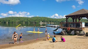 A beach with a wooden pavilion, a dock with boats, and a clear view of a lake with hills in the background. - Dayspring Cottages (Armour)
