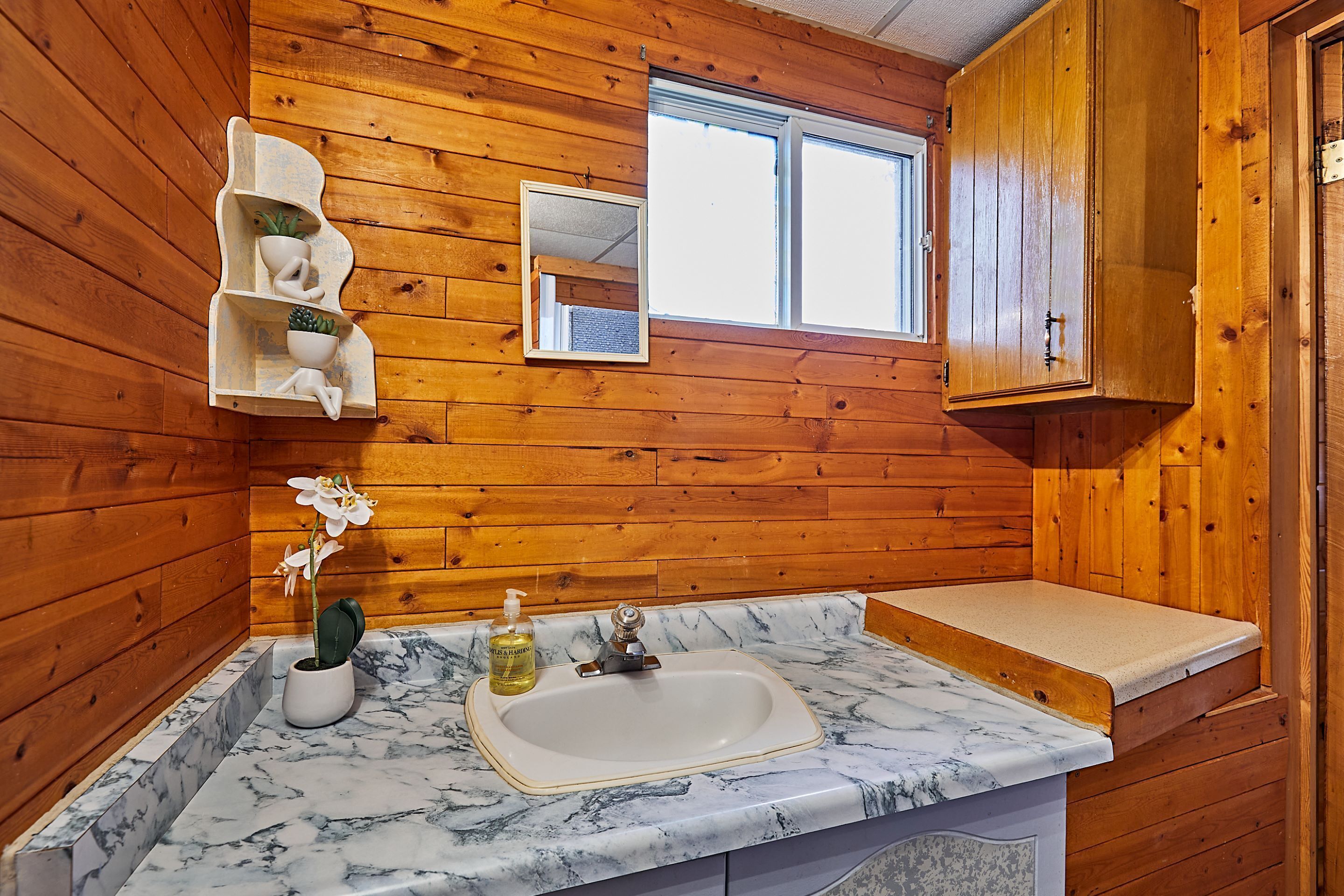 Un baño con paredes de madera, un lavamanos de mármol, un espejo y una ventana.