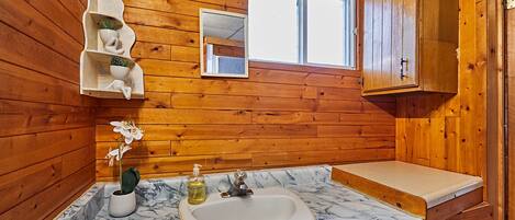 Un baño con paredes de madera, un lavamanos de mármol, un espejo y una ventana.