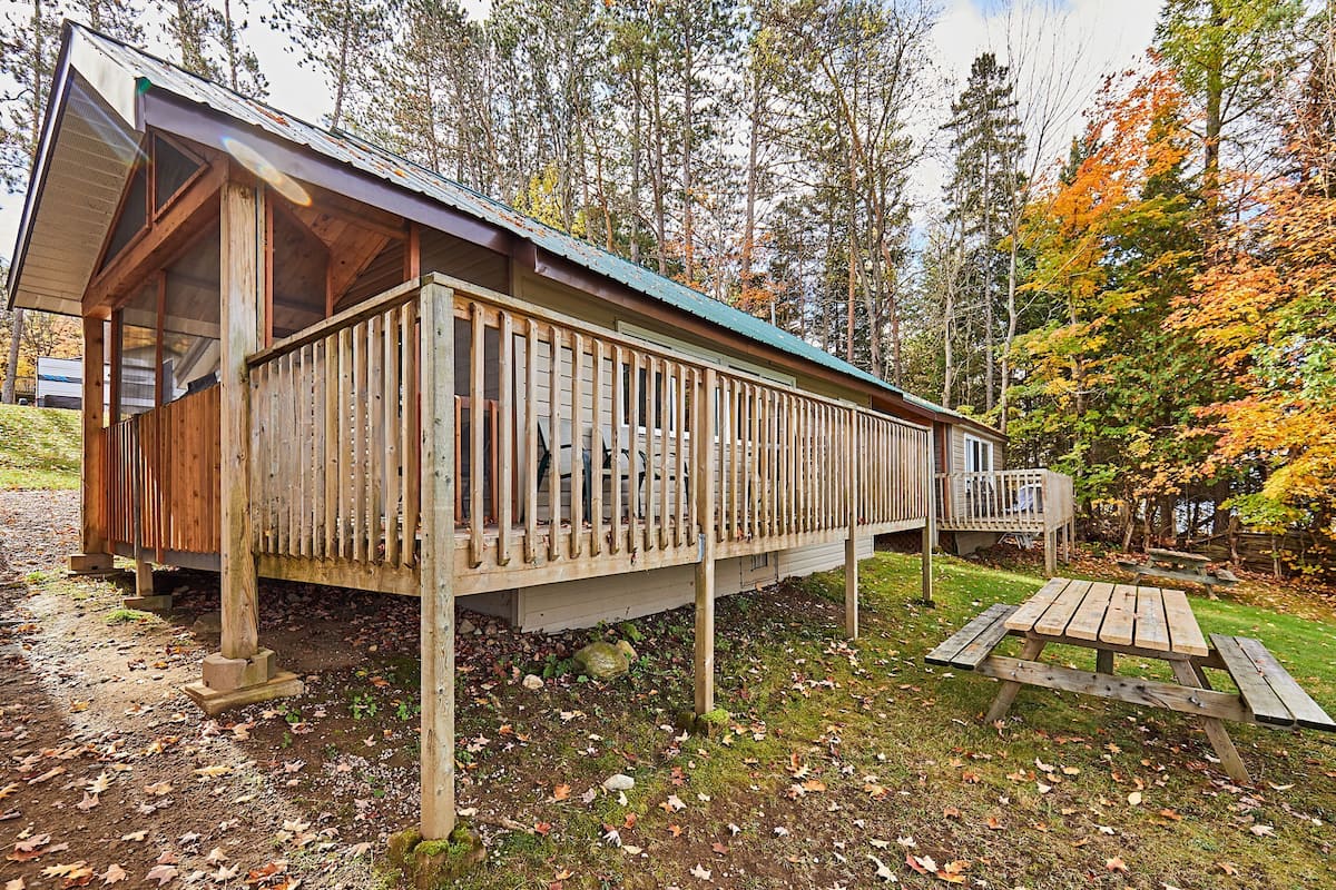 Une cabane en bois dotée d’un balcon, d’une table de pique-nique et offrant une vue sur une forêt.