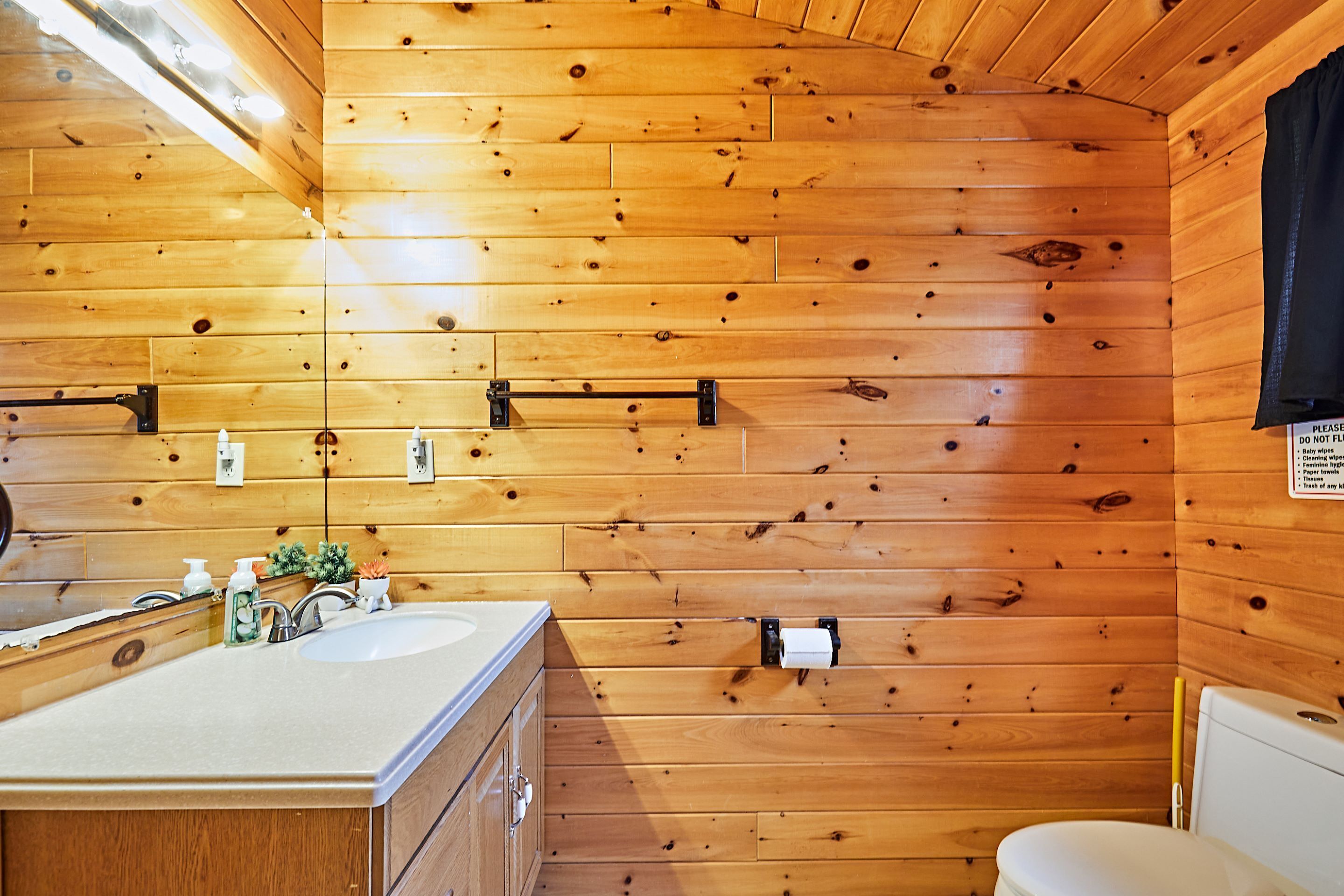 A wooden cabin bathroom with a sink, mirror, and toilet.