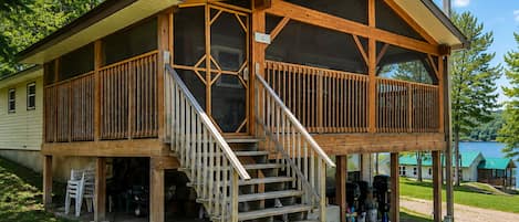 A wooden cabin with a covered porch and a staircase leading to a deck.