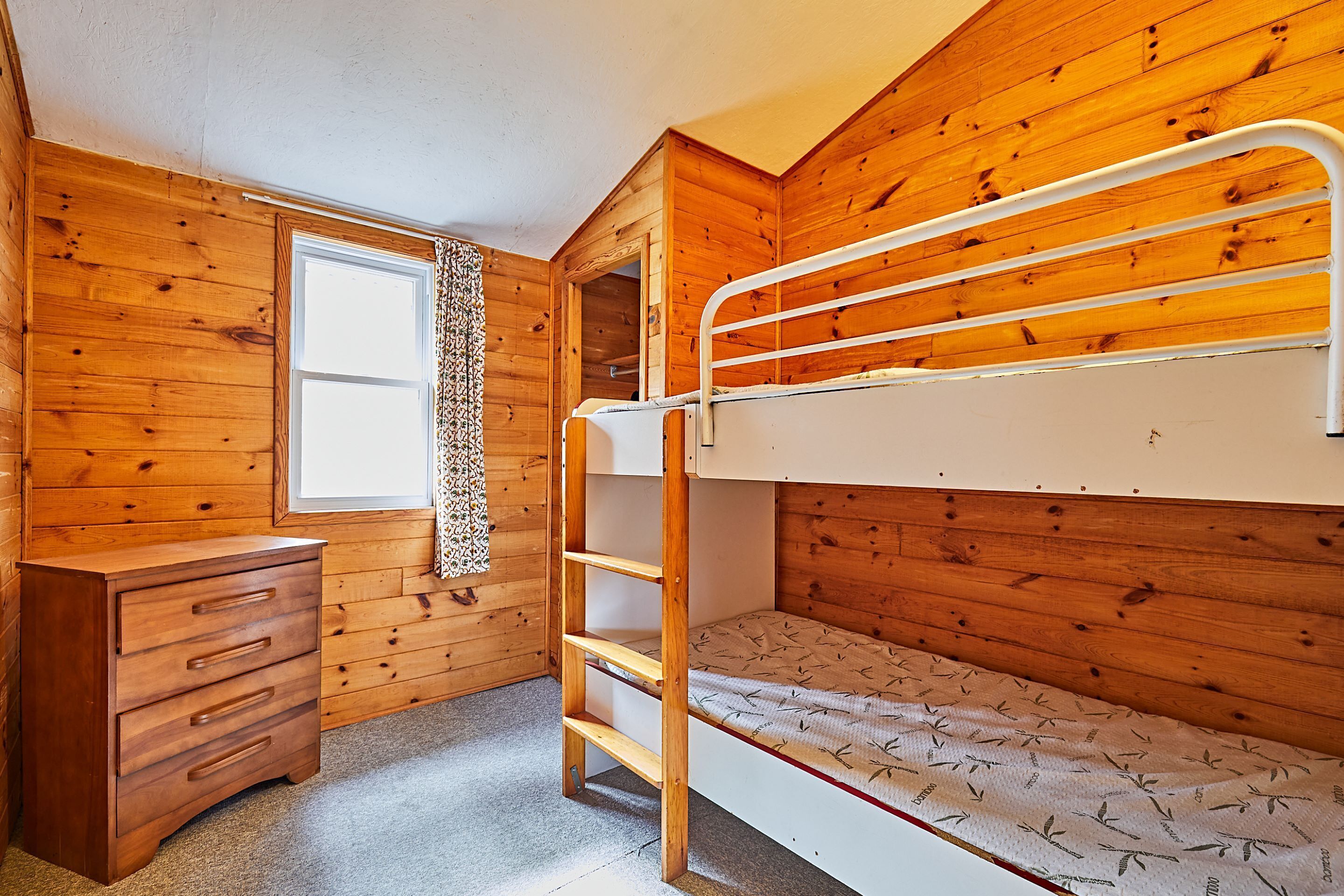 A bunk bed room with wooden walls, a window, and a wooden dresser.
