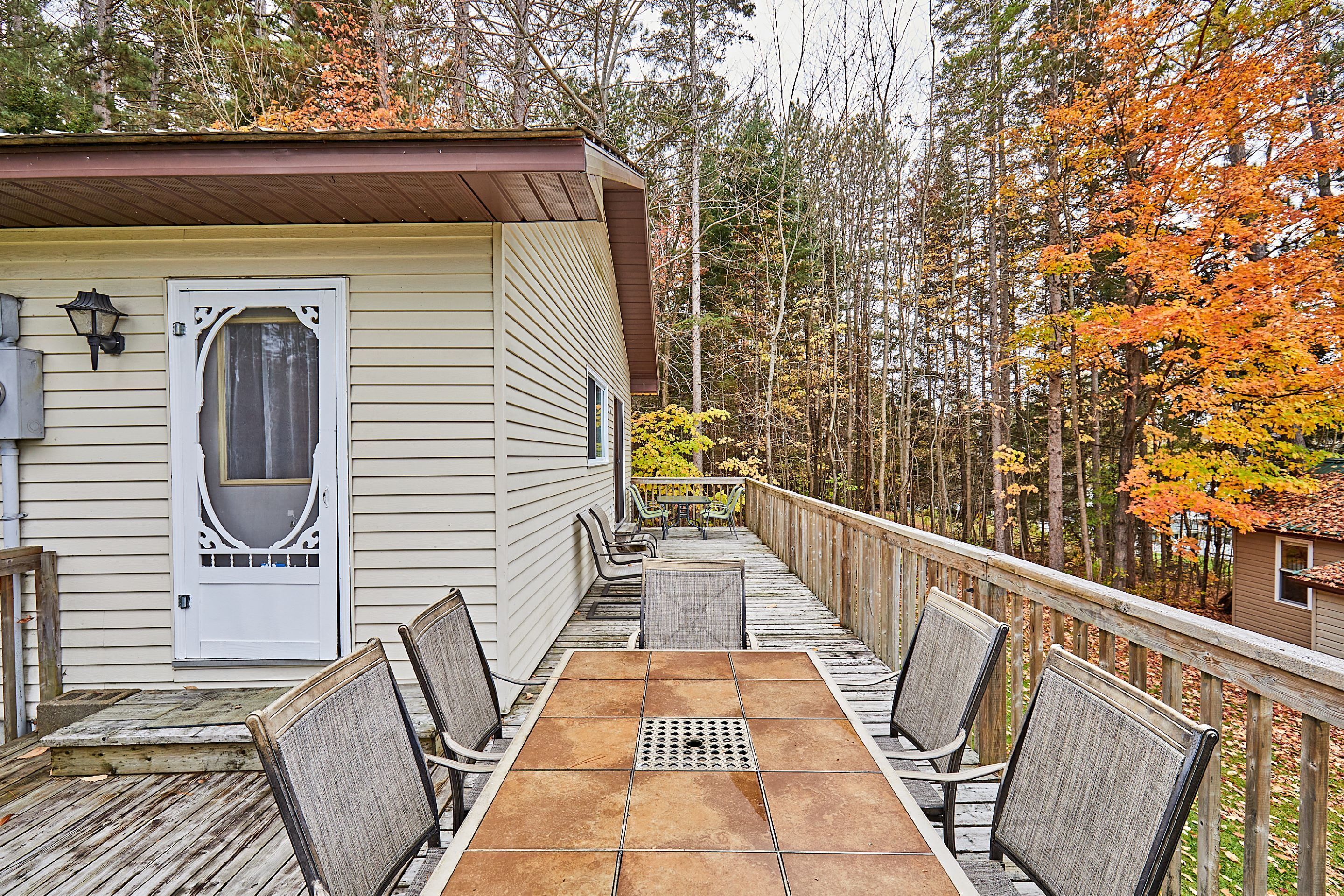 A covered deck with a table and chairs, overlooking a forested area with autumn foliage.