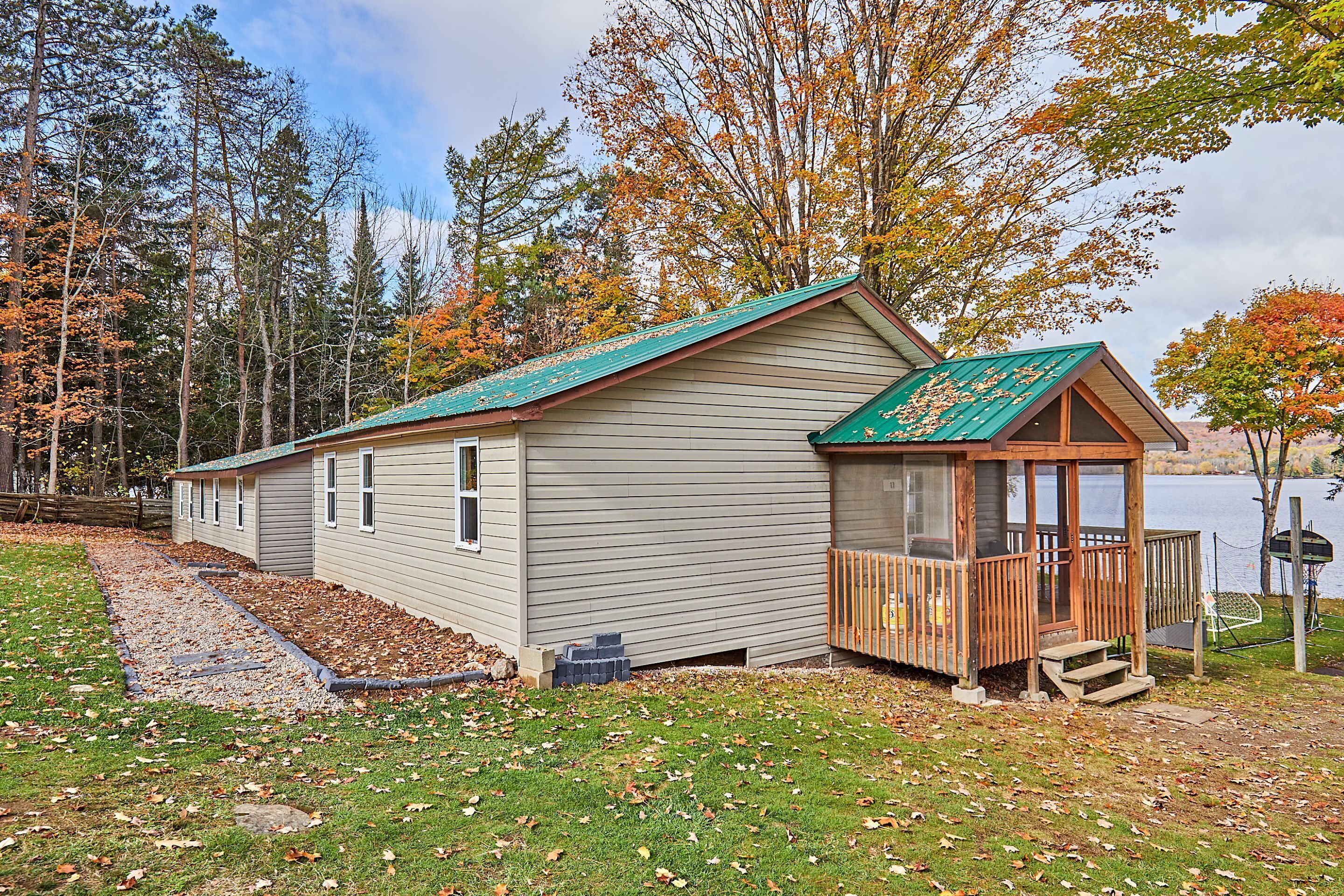 A cabin with a green roof, a wooden deck, and a view of a lake.