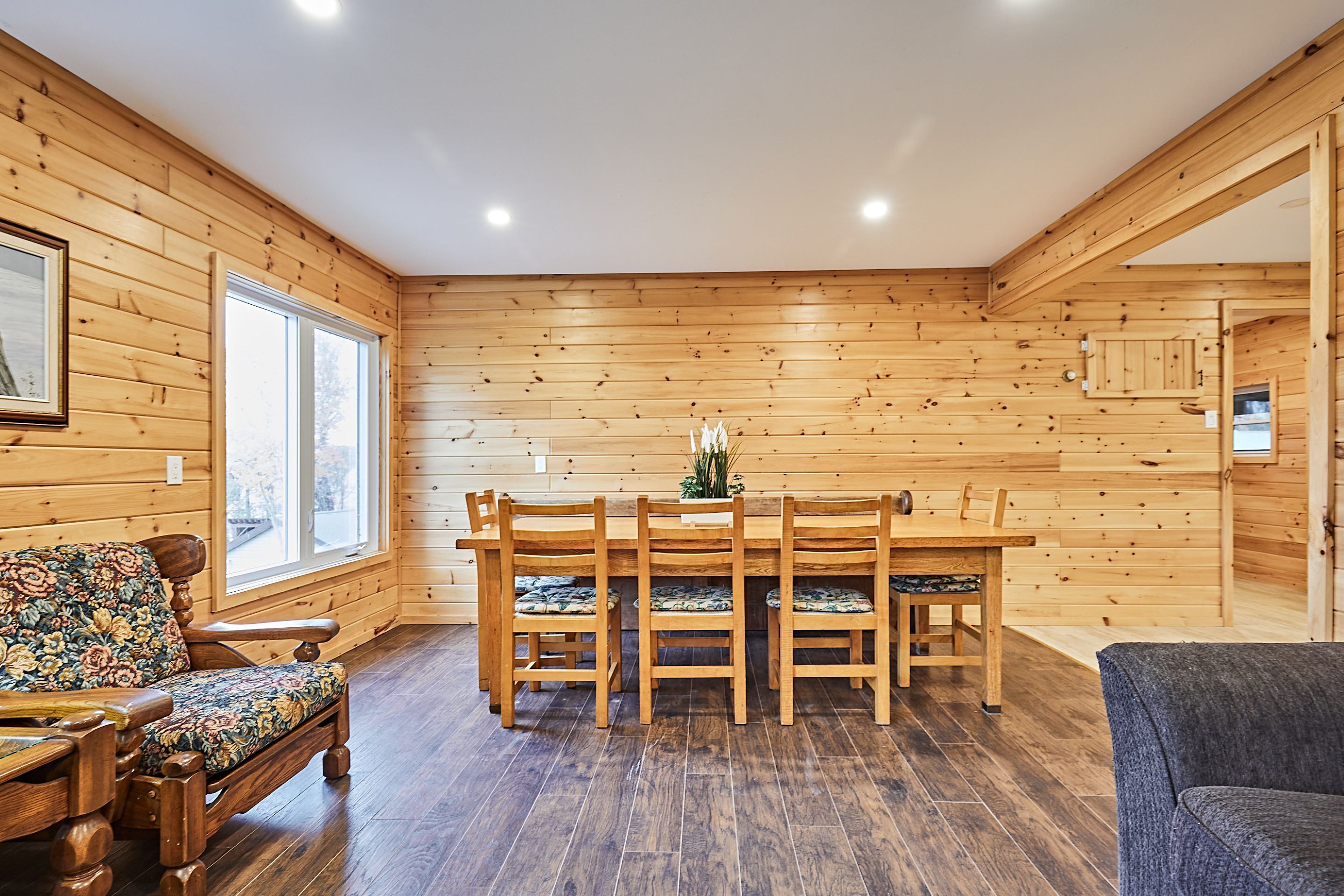 Una habitación con paneles de madera, una mesa de comedor y sillas, un sofá estampado con motivos florales, y un cuadro en la pared.