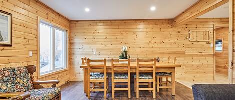 Una habitación con paneles de madera, una mesa de comedor y sillas, un sofá estampado con motivos florales, y un cuadro en la pared.