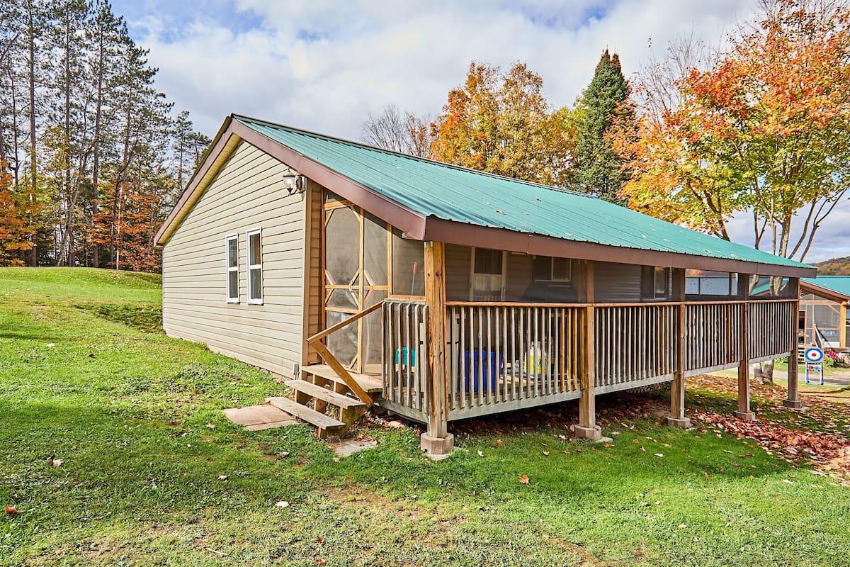 Une cabane avec une véranda, une petite terrasse et une vue sur les arbres en arrière-plan.