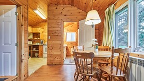 A wooden cabin interior with a dining area, kitchen, and a view through a window. - Dayspring Cottages (Armour)