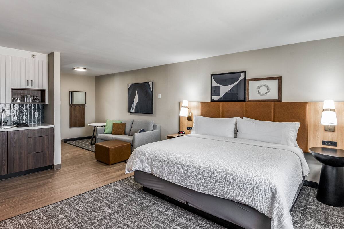 Una habitación de hotel moderna con una cama grande, un pequeño rincón de descanso, una kitchenette y un baño.