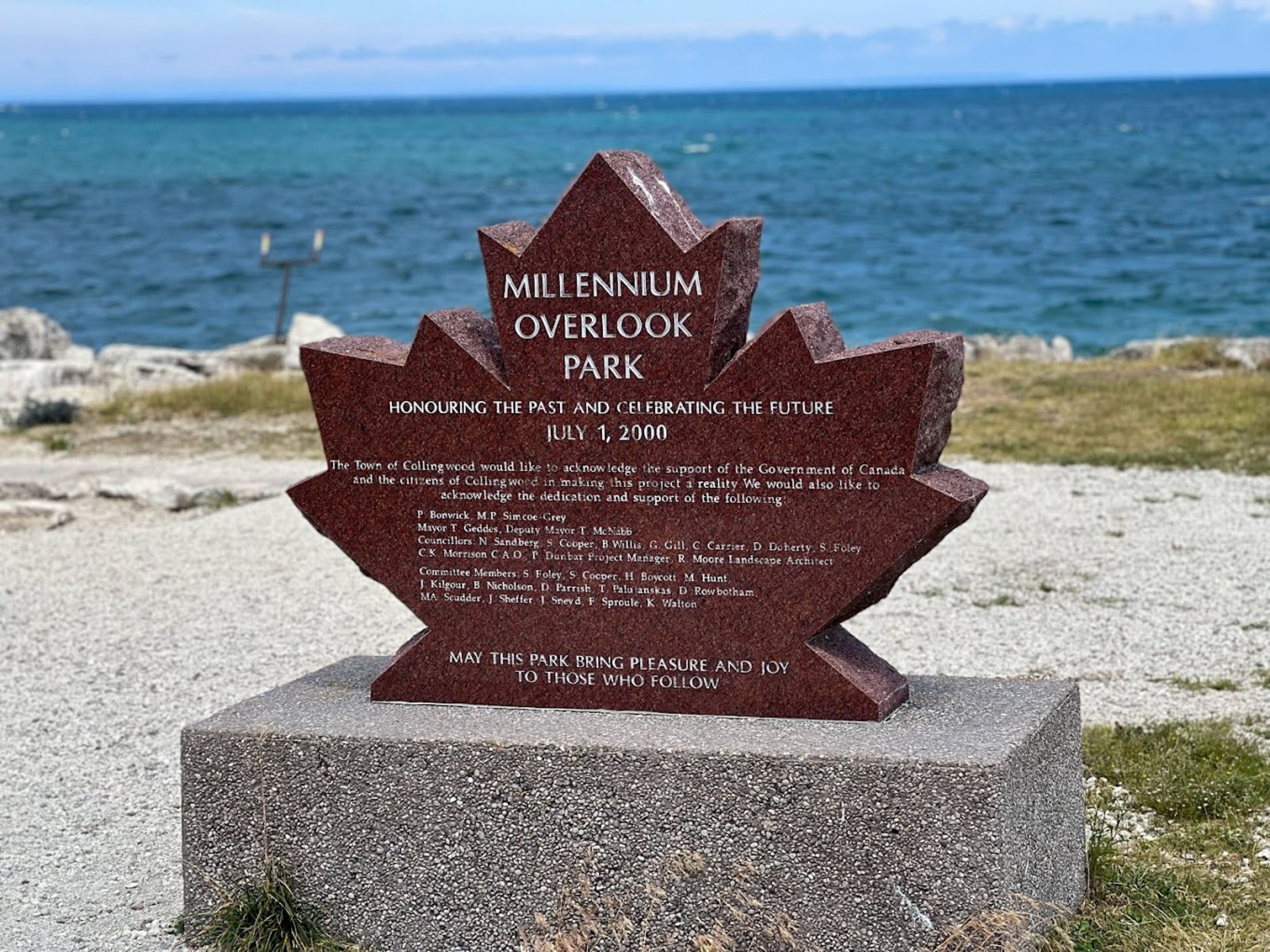A stone monument with text commemorating Millennium Overlook Park, dedicated on July 1, 2000, with a view of the ocean in the background.