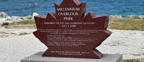 A stone monument with text commemorating Millennium Overlook Park, dedicated on July 1, 2000, with a view of the ocean in the background.