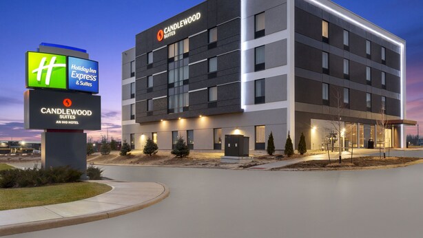 Een modern hotelgebouw met een Holiday Inn Express bord, de naam Candlewood Suites, en een goed verlichte ingang.