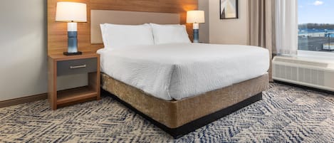 A hotel room with a large bed, two bedside lamps, a nightstand, a window with a view, and a framed picture on the wall.