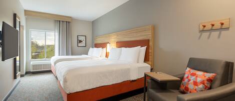 A hotel room with a large bed, a desk, a chair, and a TV mounted on the wall.